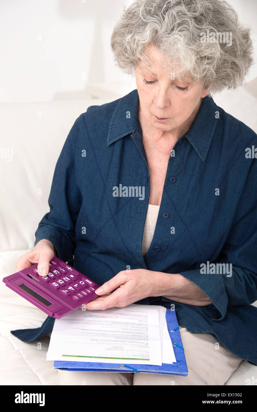 -MODELL VERÖFFENTLICHT. Ältere Frau mit einem Taschenrechner mit Papierkram. Stockfoto