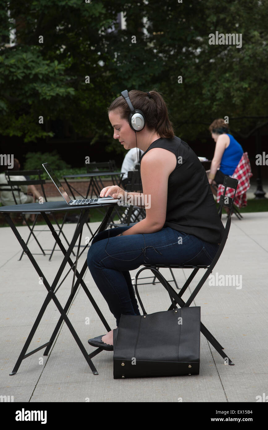 Schüler arbeiten sitzen an einem Metall Tisch arbeiten im Freien auf einem Computer mit Kopfhörern Stockfoto