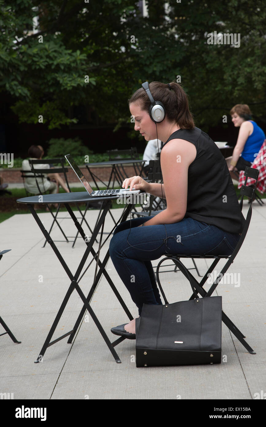 Schüler arbeiten sitzen an einem Metall Tisch arbeiten im Freien auf einem Computer mit Kopfhörern Stockfoto
