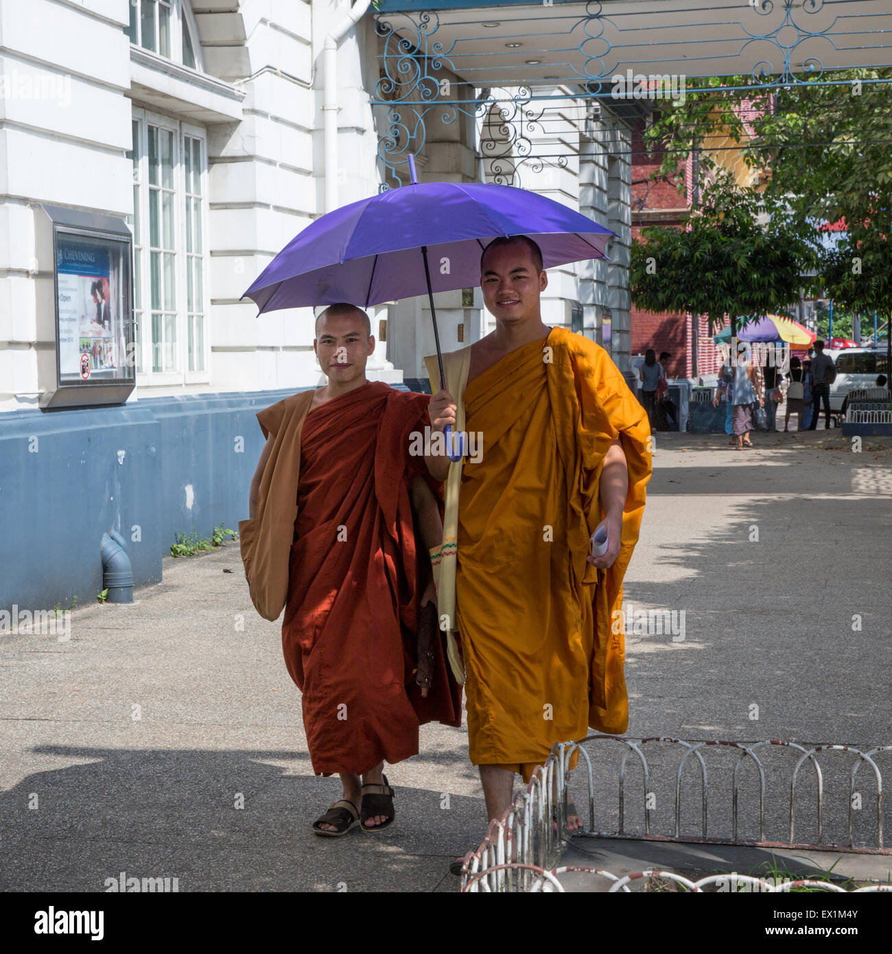 Zwei buddhistische Mönche in typischen Safran Roben zu Fuß unter einem Sonnenschirm am Strand in Yangon Myanmar Stockfoto