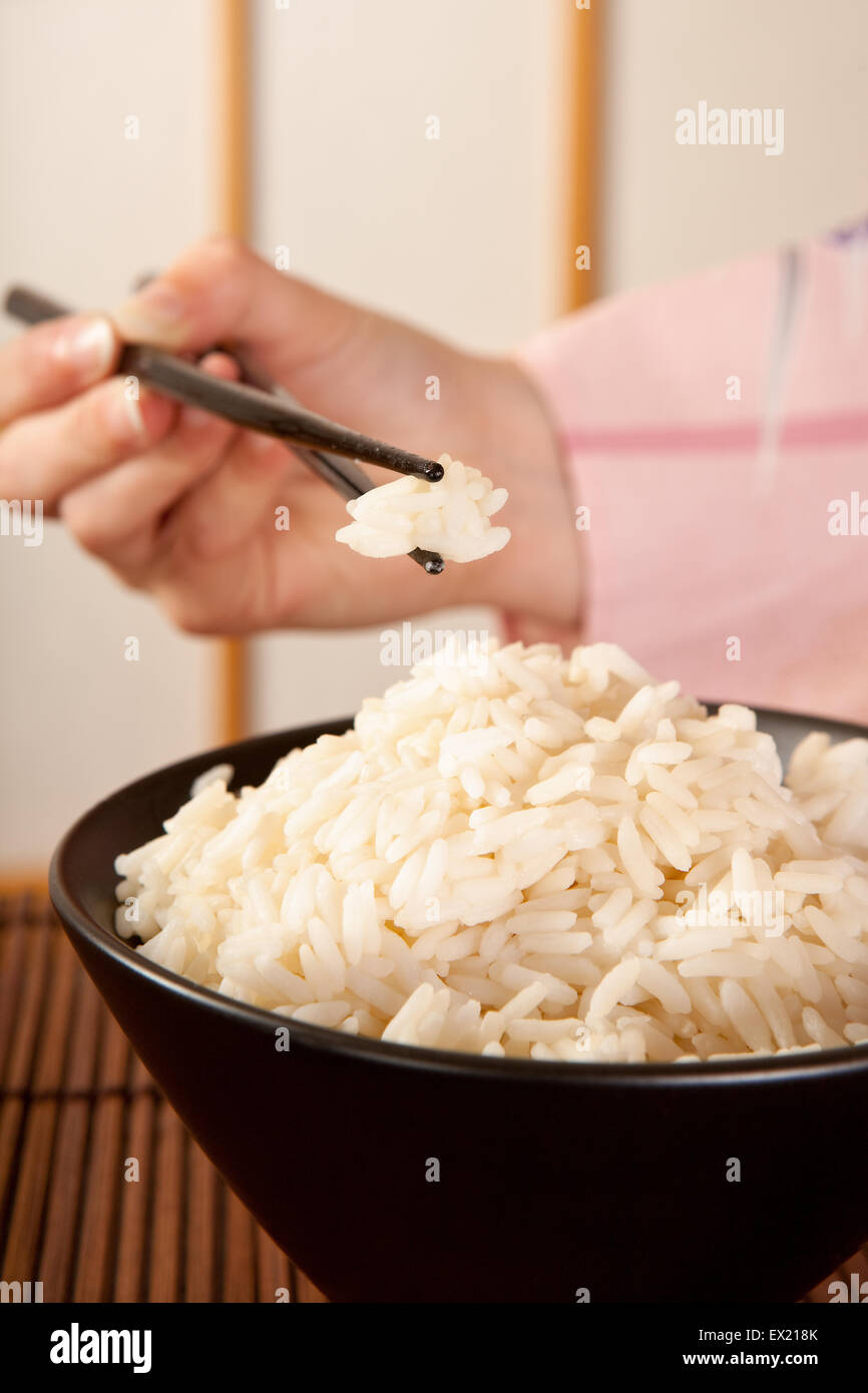 Hände in Kimono Ärmel halten Reis mit Stäbchen vor einem japanischen Shoji-Schiebefenster Stockfoto