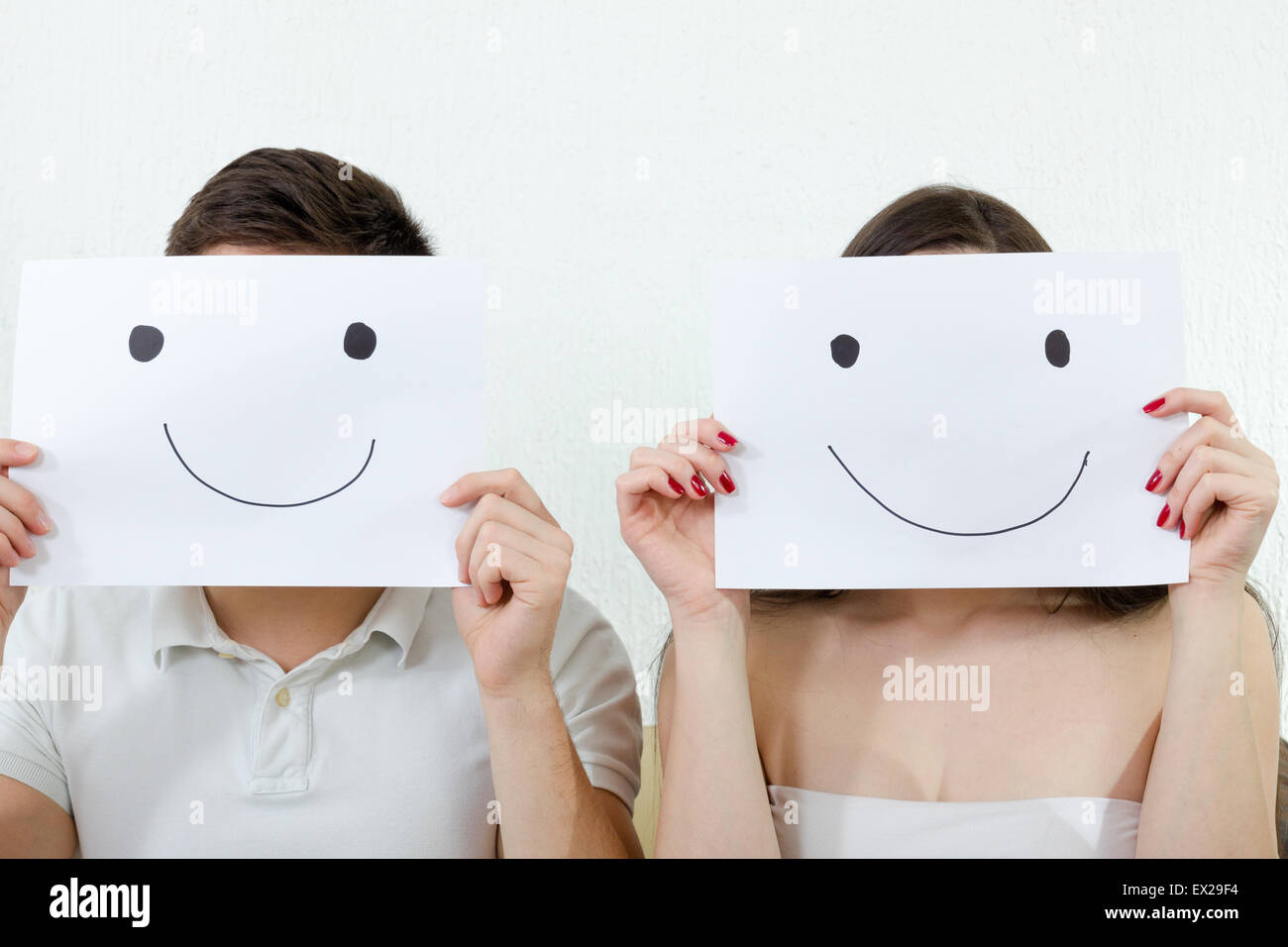 Glückliches Paar Smileys über ihre Gesichter beim Sitzen auf der Couch im Wohnzimmer zu halten. Paar decken ihre Gesichter mit happy Stockfoto