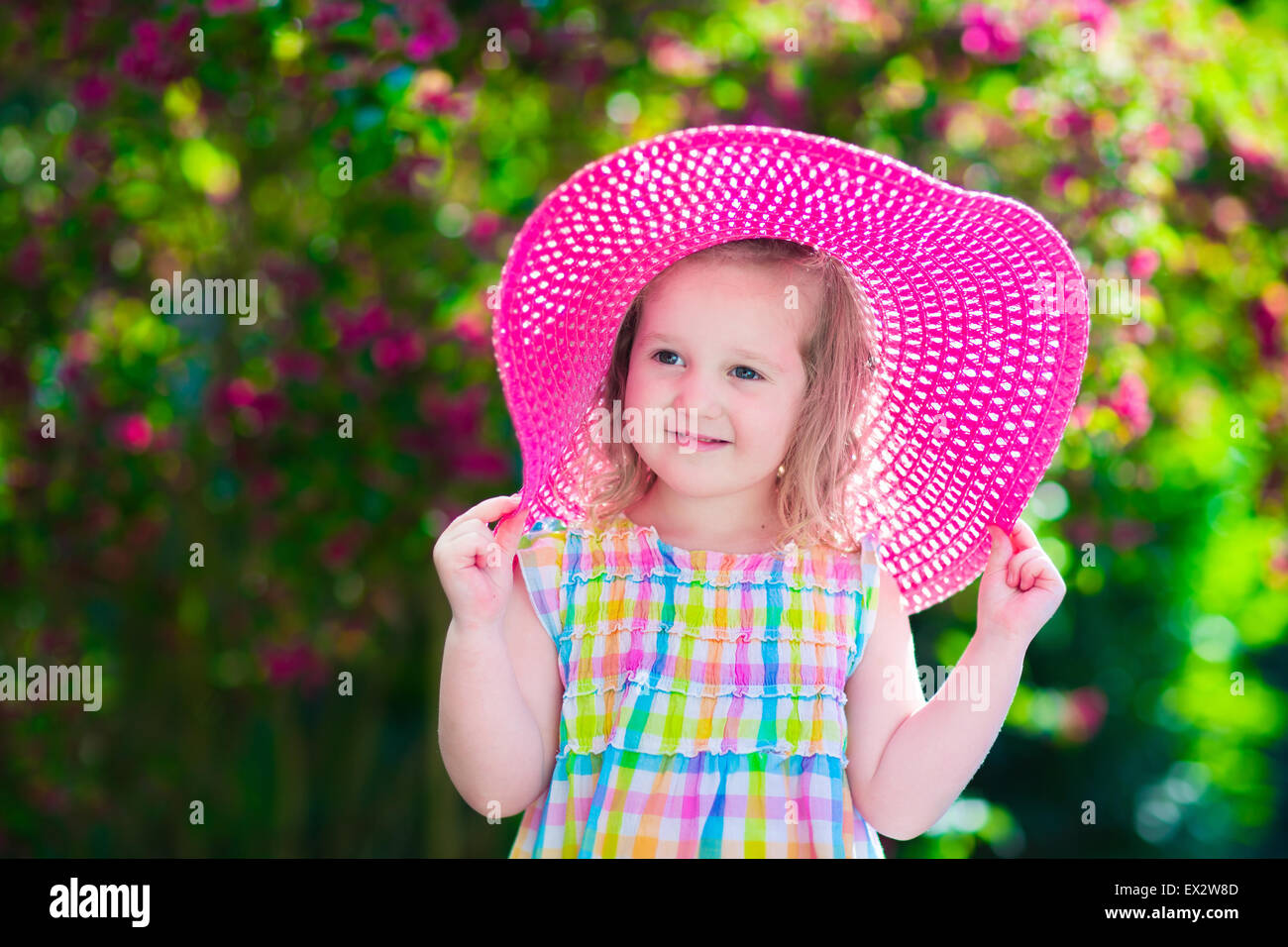 Kleine süße Mädchen mit Blumen. Kind einen rosa Hut spielen in einem blühenden Sommer Garten. Kinder im Garten. Stockfoto