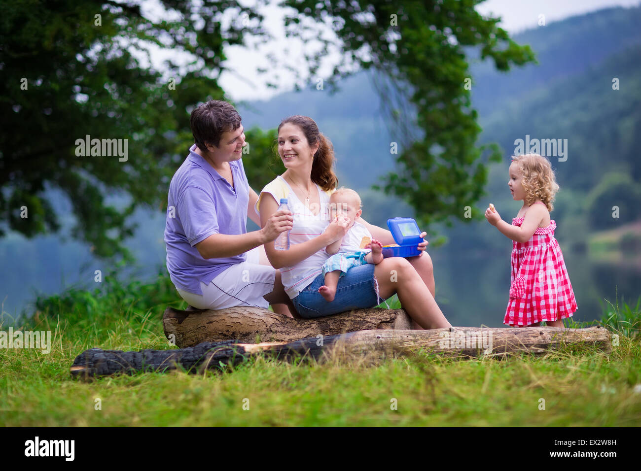 Familie auf Sommerwanderung. Junge Eltern mit Kindern wandern an einem See. Mutter, Vater und zwei Kinder haben Picknick im Freien. AC Stockfoto
