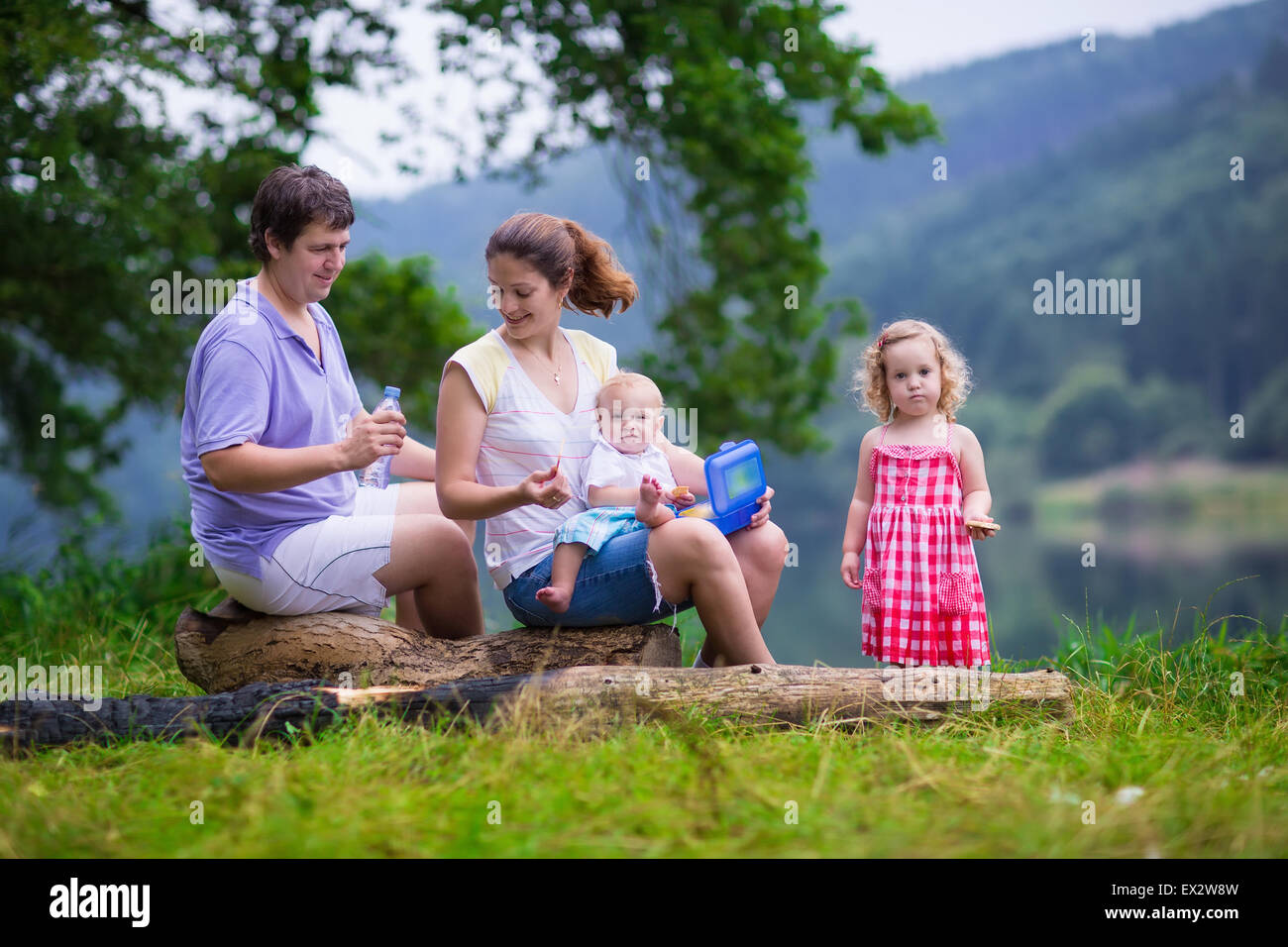 Familie auf Sommerwanderung. Junge Eltern mit Kindern wandern an einem See. Mutter, Vater und zwei Kinder haben Picknick im Freien. Stockfoto