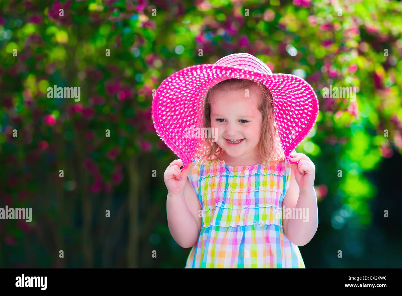 Kleine süße Mädchen mit Blumen. Kind einen rosa Hut spielen in einem blühenden Sommer Garten. Kinder im Garten. Kinder spielen zu übertreffen Stockfoto