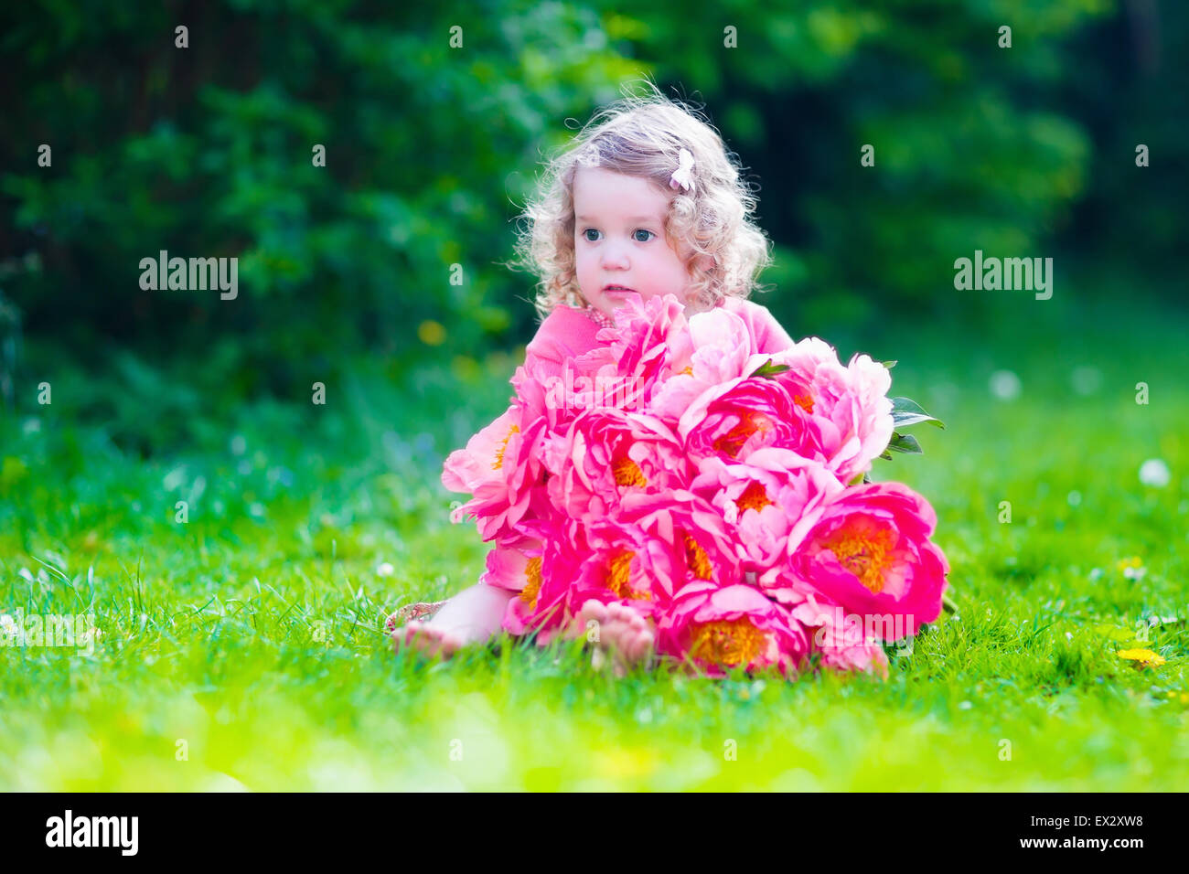 Kleine süße Mädchen mit Pfingstrosen Blumen. Das Kind trägt ein rosa Kleid spielen im Sommergarten. Kinder im Garten. Stockfoto