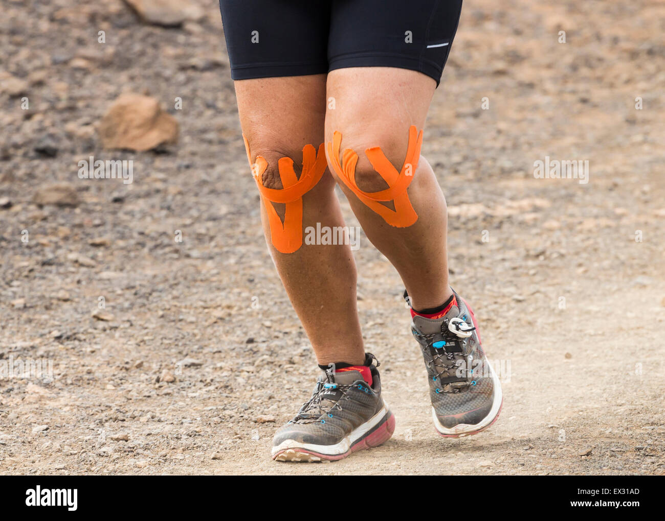 Starke weibliche Läufer tragen elastisches therapeutische Tape (KT Tape, Kinesiologie Tape...) auf Knien während der Trail Rennen Stockfoto