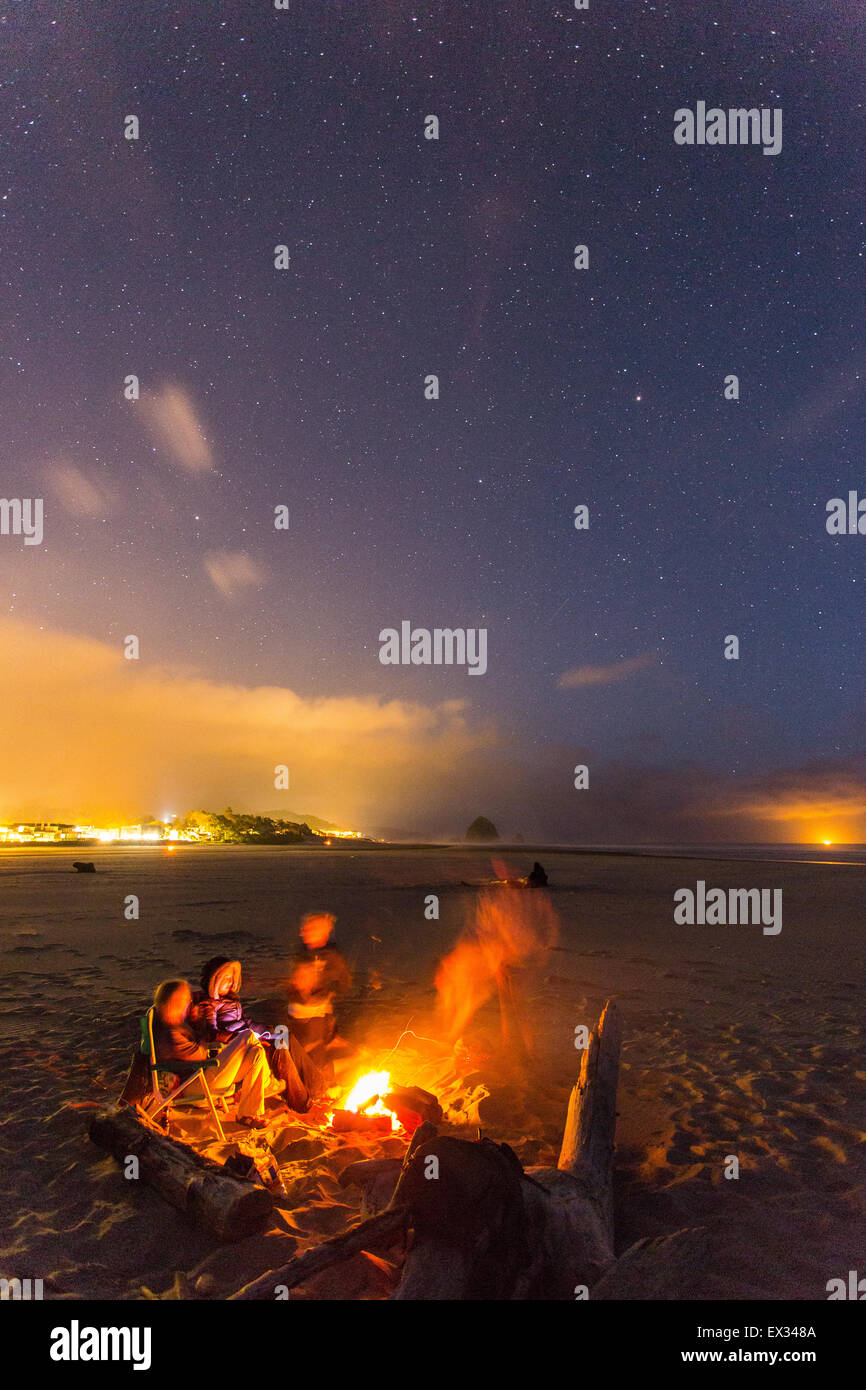 Freunde versammeln sich um ein Strand-Lagerfeuer unter dem Sternenhimmel in Cannon Beach, Oregon. Stockfoto
