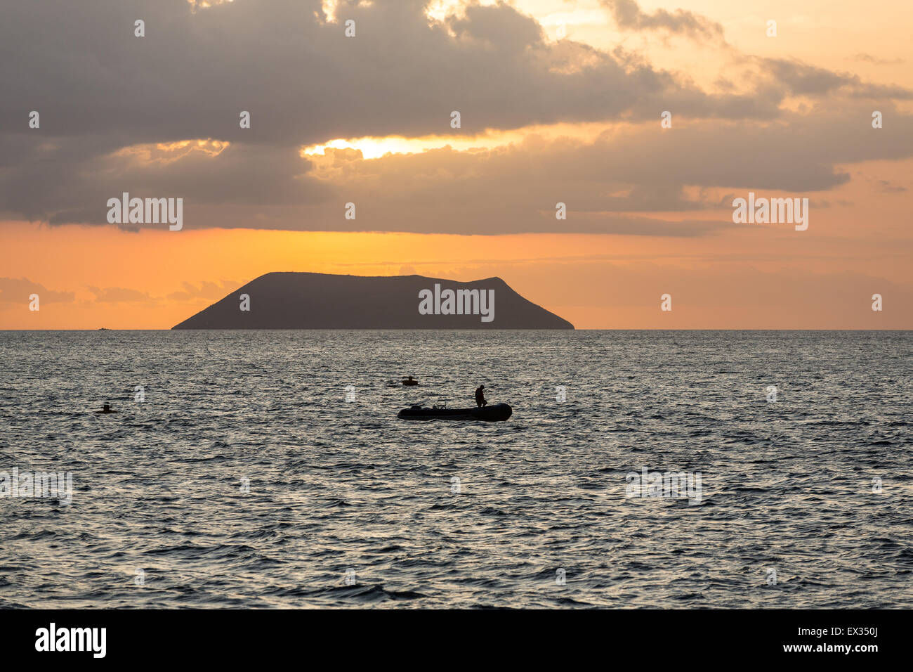 Ein Fährmann ist gegen die untergehende Sonne und einen kleinen Vulkan aus North Seymour auf den Galapagos Inseln Silhouette. Stockfoto