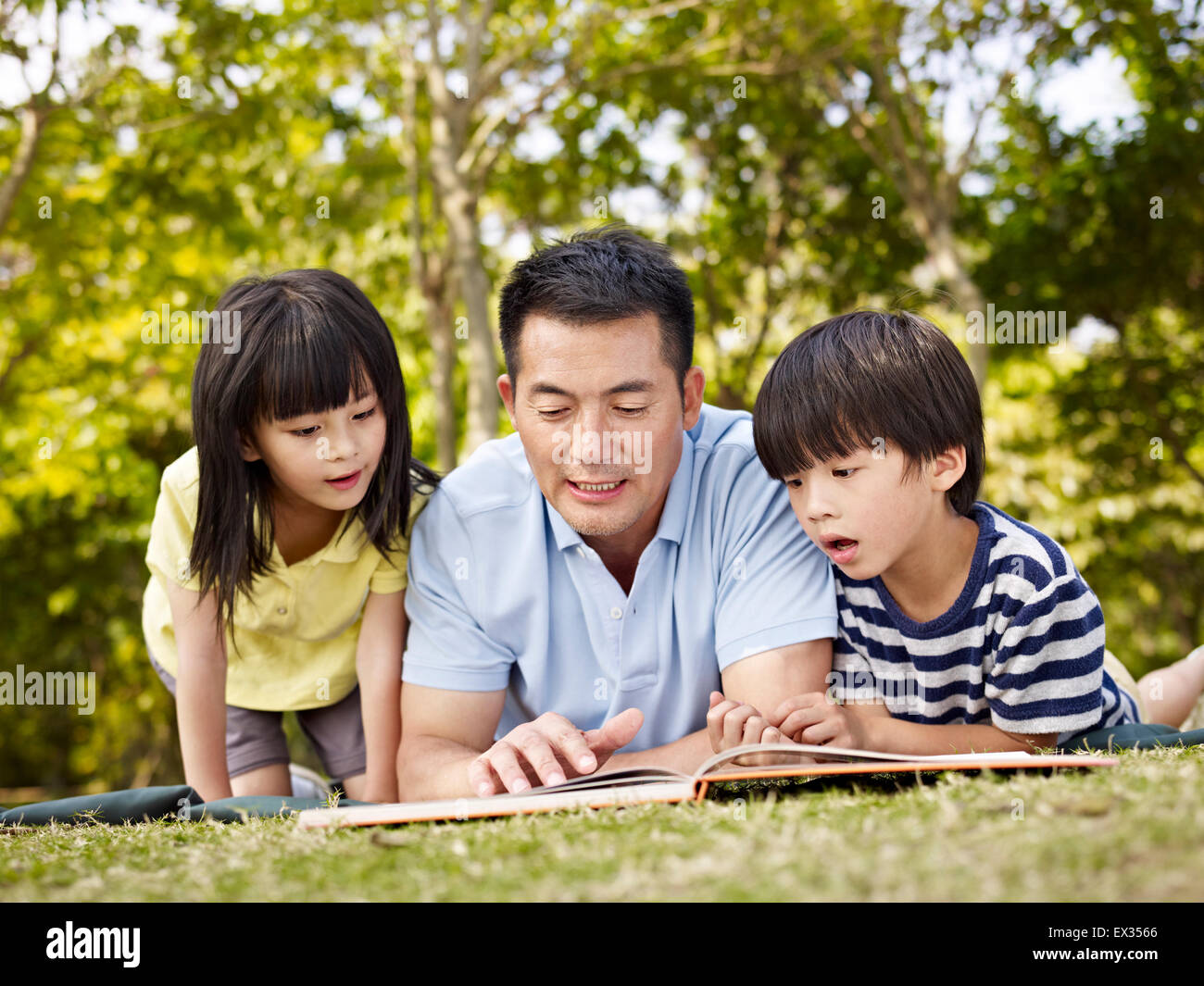 Vater und Kinder lesen ein Buch im Freien. Stockfoto