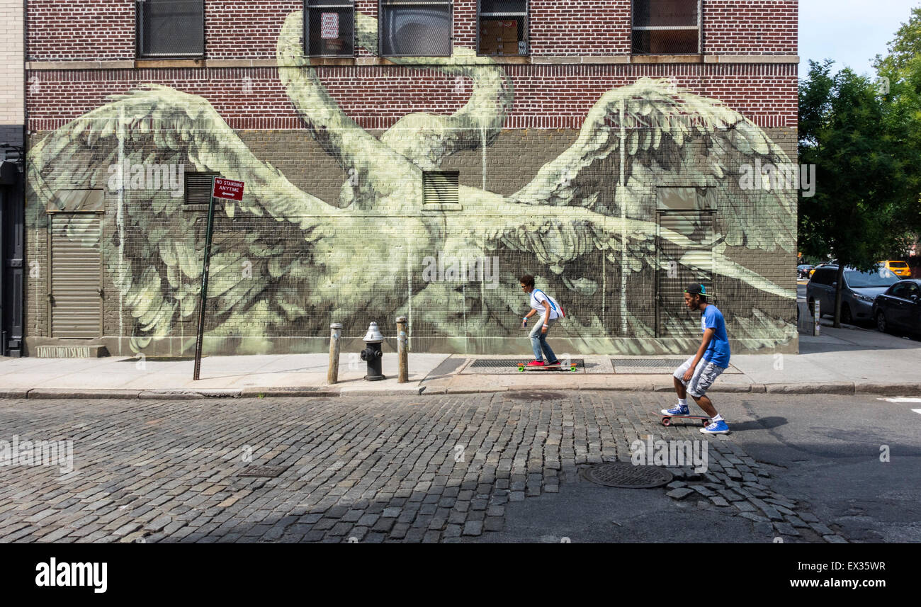Ein junges multiethnische paar skateboarding übergeben eine große street-Art-Wandbild der Paarung Schwäne, Lower East Side in New York City Stockfoto