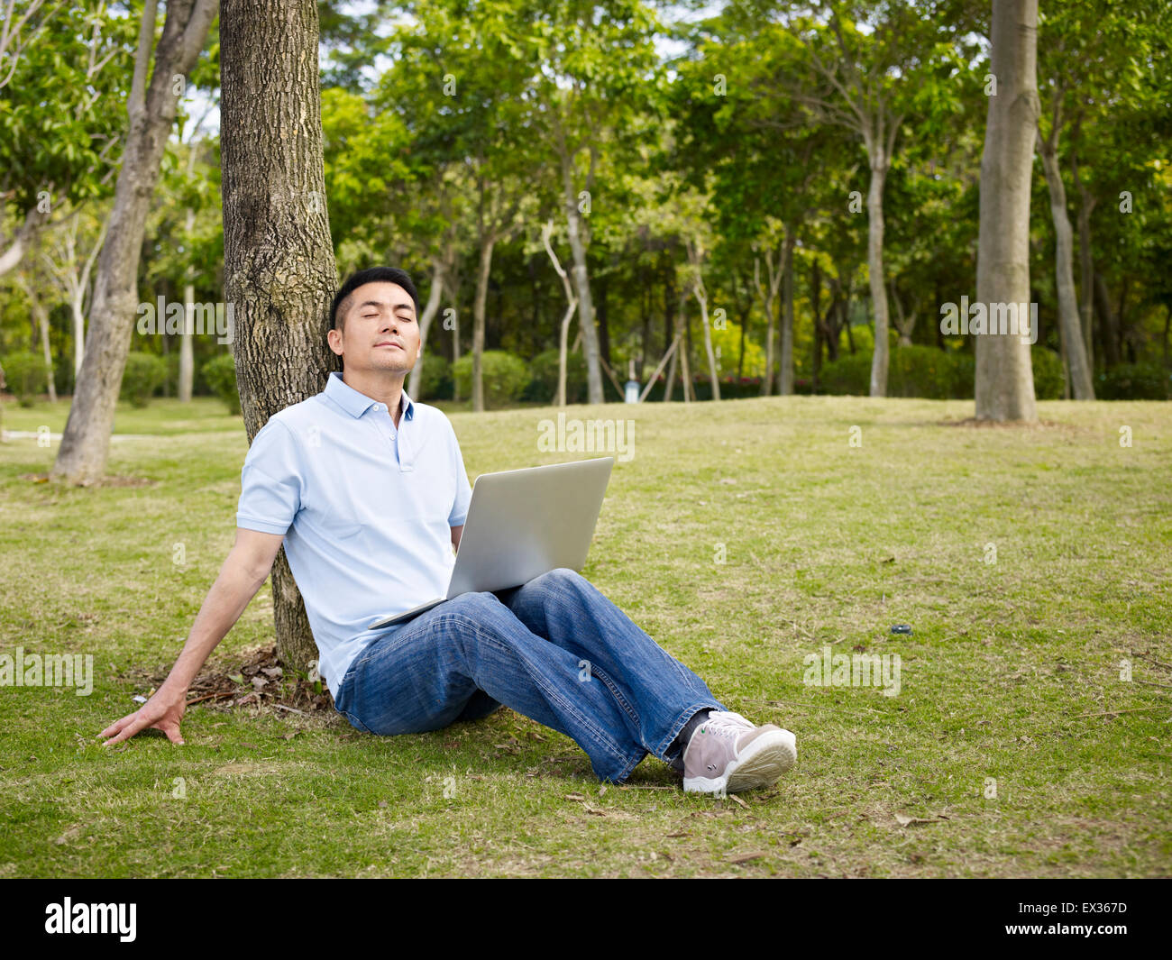 asiatischer Mann in lässig tragen mit Laptop-Computer im Freien im Park. Stockfoto