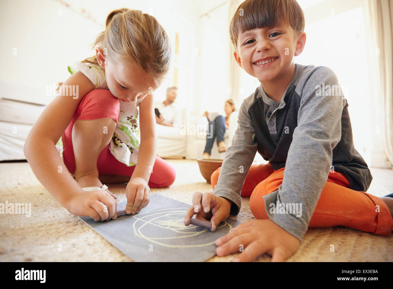 Innenaufnahme der gerne kleine Kinder, die Zeichnung und Färbung auf Boden mit Eltern im Hintergrund zu Hause sitzen Stockfoto