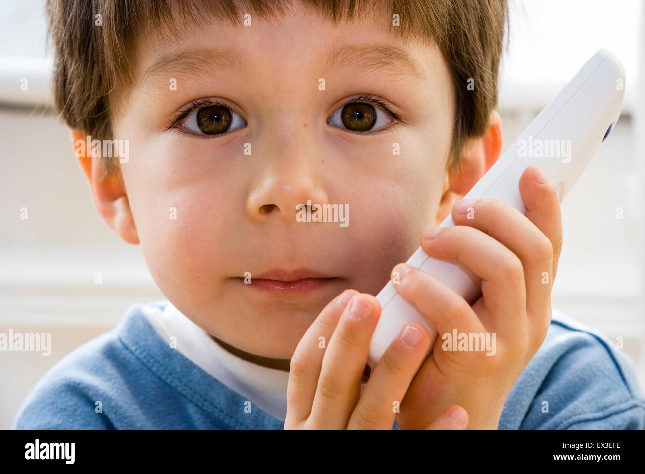 Nahaufnahme von einem kaukasischen Kind, Junge, 5-6 Jahre alt, Verlegung im Innenbereich auf Holzboden holding Telefon an sein Ohr, die versuchen, die Lautsprecher zu hören. Auge - Kontakt. Stockfoto