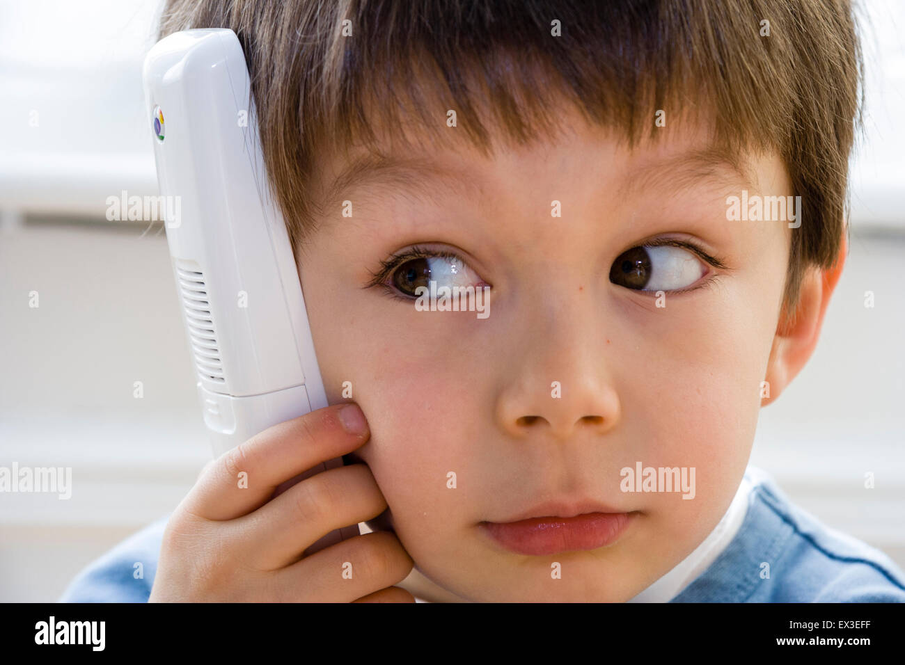 Nahaufnahme von einem kaukasischen Kind, Junge, 6-7 Jahre alt, Verlegung im Innenbereich auf Holzboden holding Telefon an sein Ohr, die versuchen, die Lautsprecher zu hören. Stockfoto