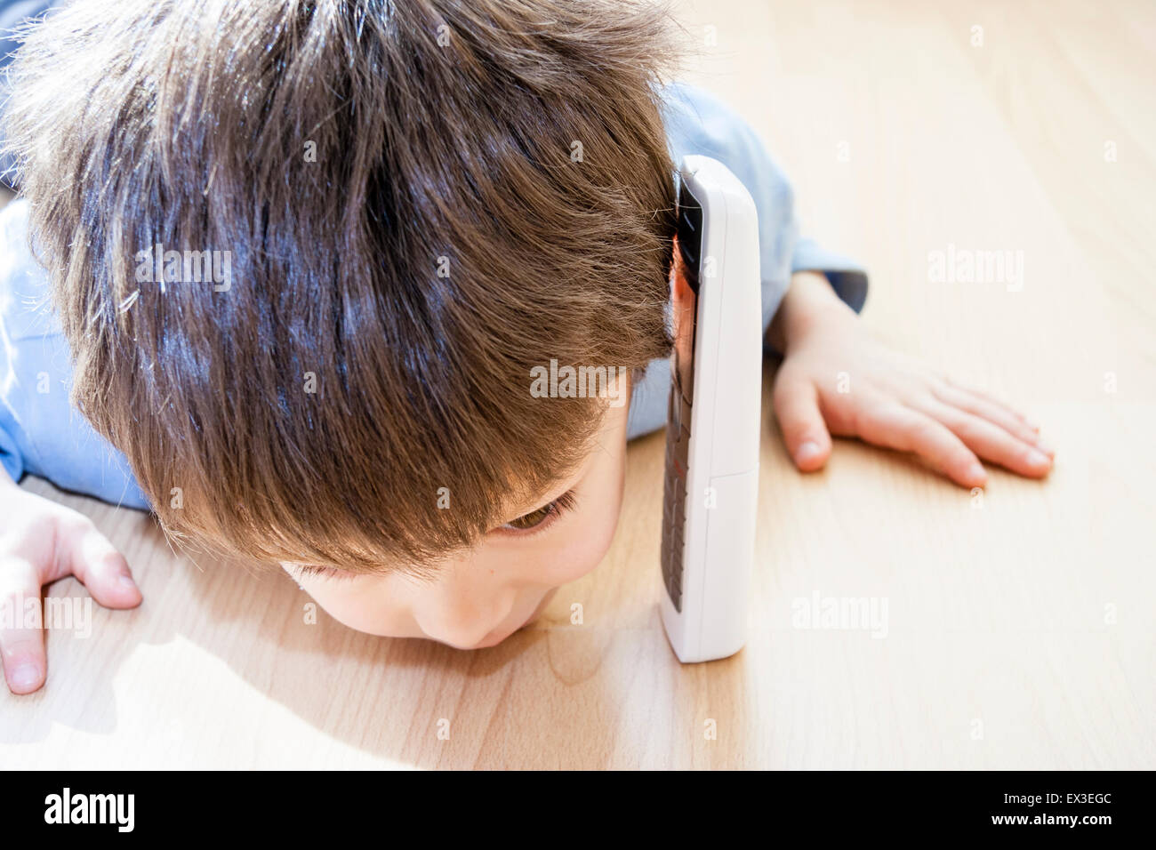 Nahaufnahme von einem kaukasischen Kind, Junge, 6-7 Jahre alt, Verlegung im Innenbereich auf Holzboden mit seinem Ohr gegen eine frei stehende Telefon und versuchte, zu hören. Stockfoto