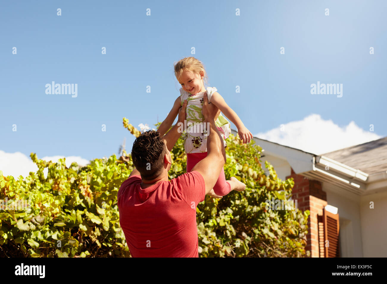 Junger Mann seiner Tochter hoch in die Luft heben. Glücklicher Vater und Tochter spielen in ihrem Hinterhof an einem sonnigen Tag. Stockfoto