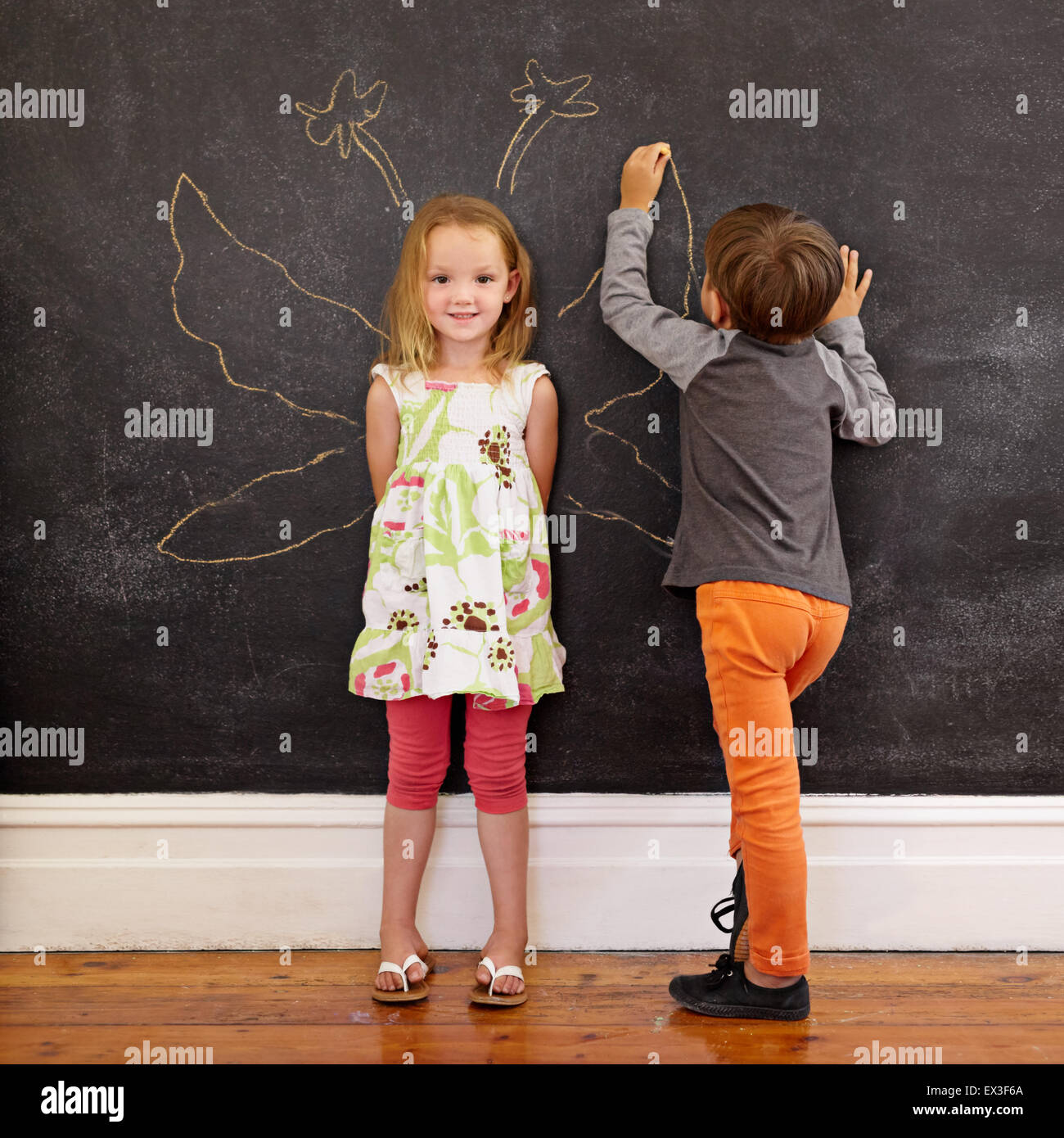 In voller Länge Portrait von niedliche kleine Mädchen stehen und kleiner Junge Engelsflügel um sie herum auf Tafel zeichnen. Stockfoto