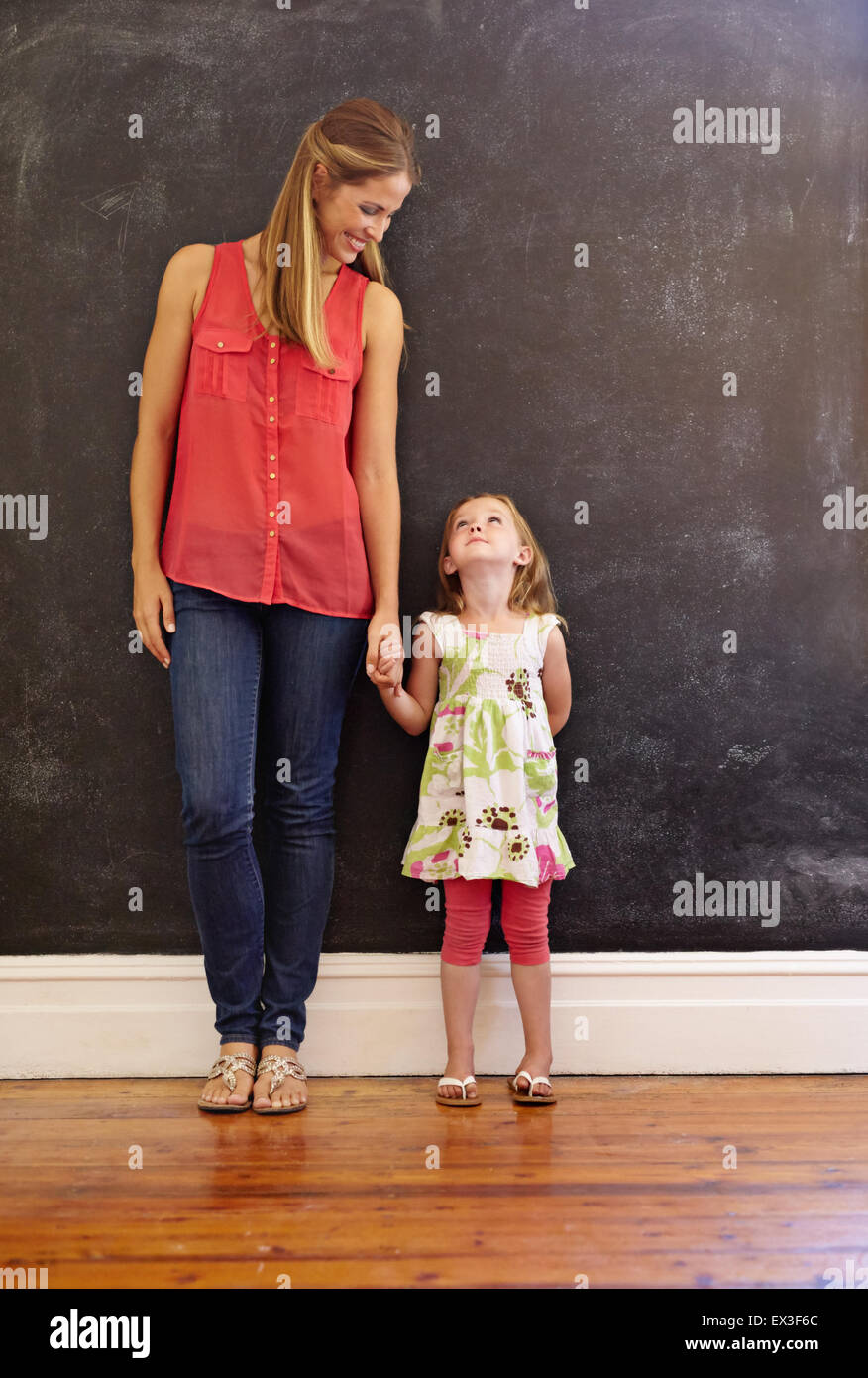 Voller Länge Schuss süße kleine Mädchen mit ihrer Mutter zu Hause stehen. Mutter und Tochter sahen einander an einer Wand Stockfoto