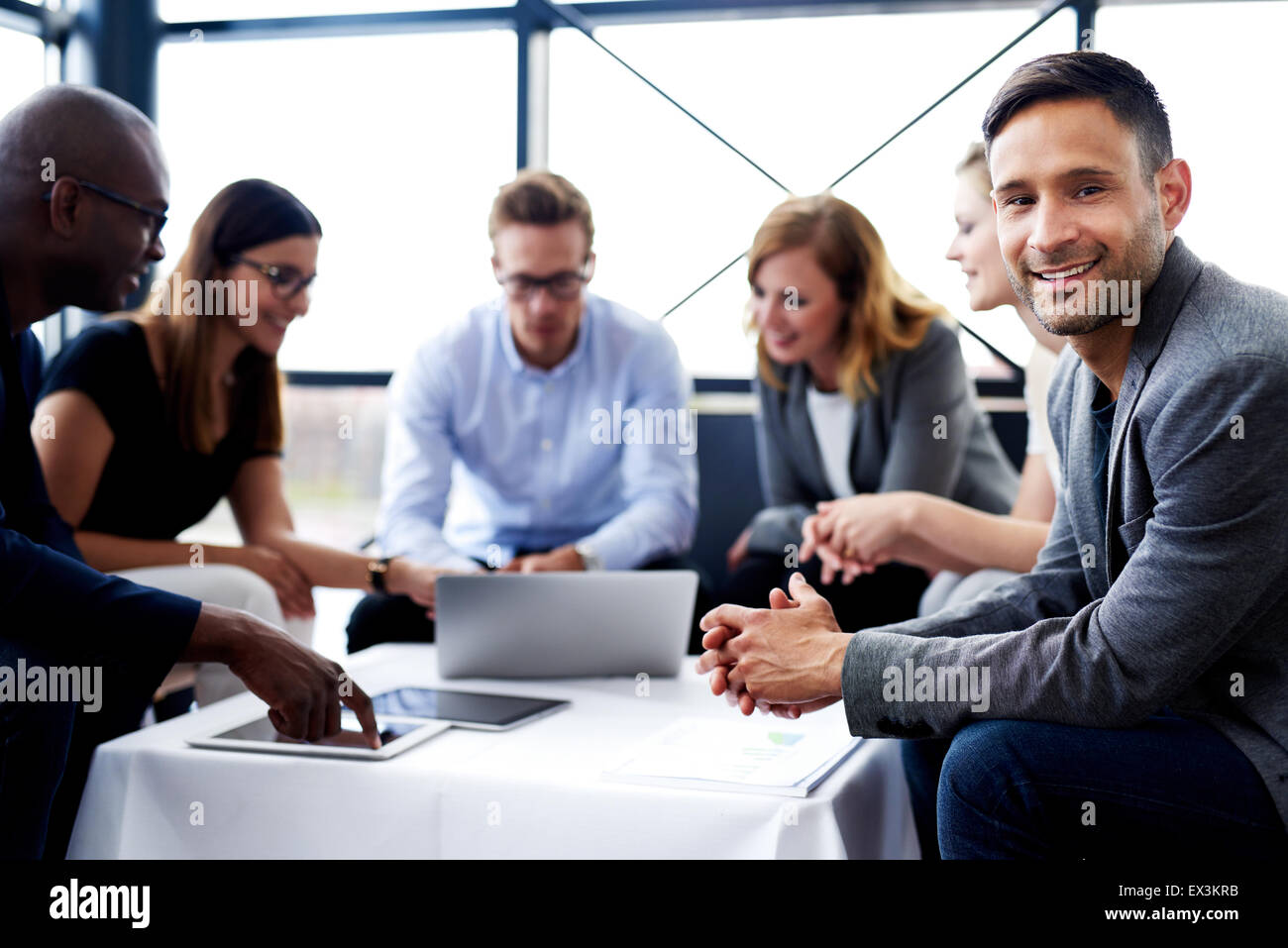 Weißen männlichen executive sitzen und Lächeln in die Kamera während eines Meetings mit Kollegen Stockfoto