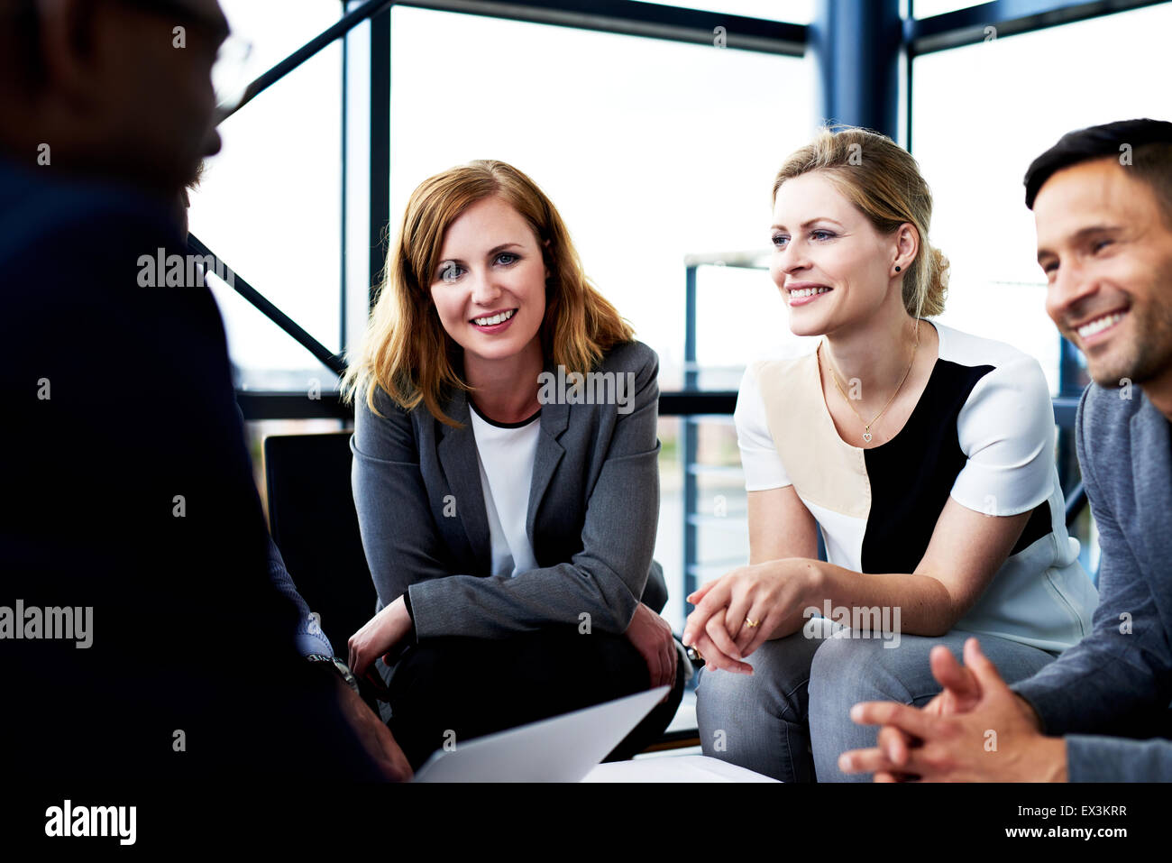 Weibliche Weiße executive Lächeln auf die Kamera nach vorn gelehnt Knien sitzt neben Kollegen Stockfoto