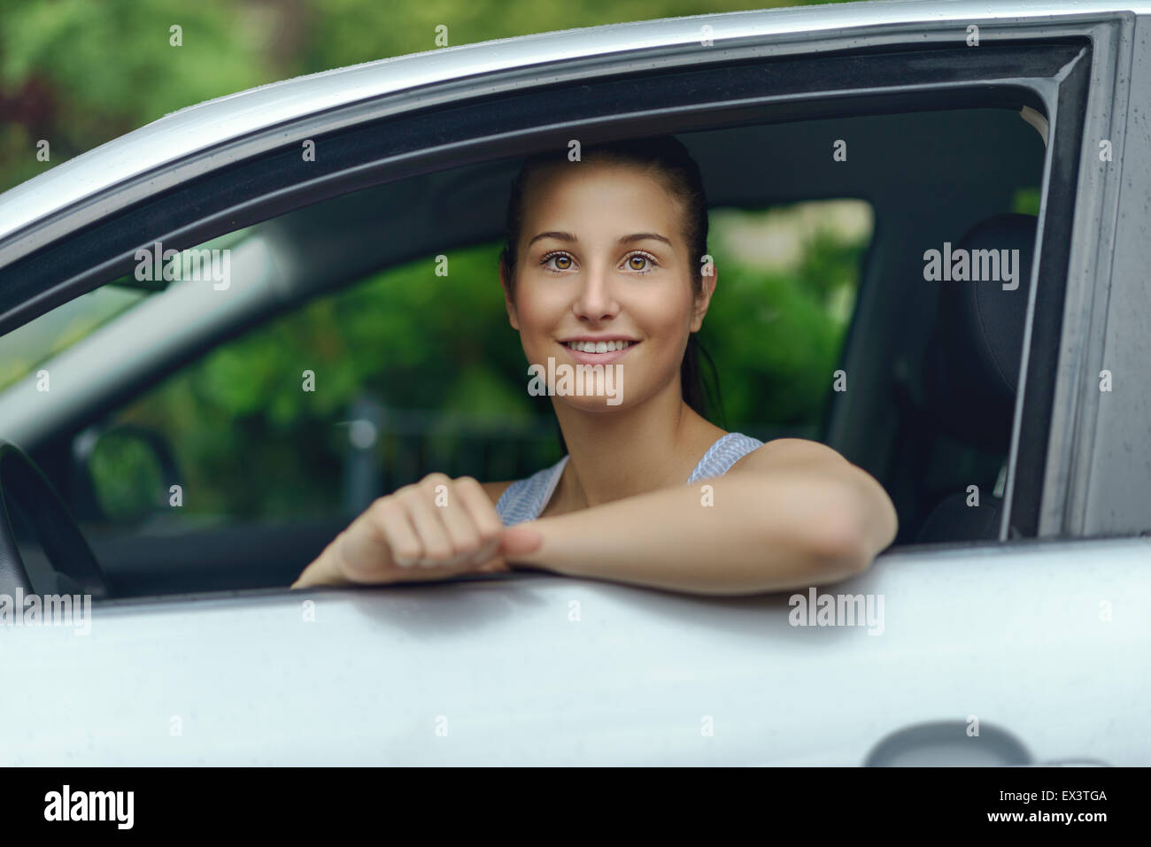 Hübsche junge Frau sitzt im Auto, während stützte sich auf das offene Fenster in die Kamera Lächeln Stockfoto