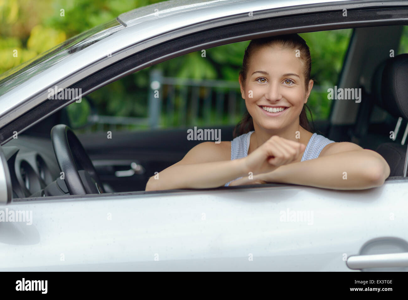 Hübsche junge Frau sitzt im Auto, während stützte sich auf das offene Fenster in die Kamera Lächeln Stockfoto