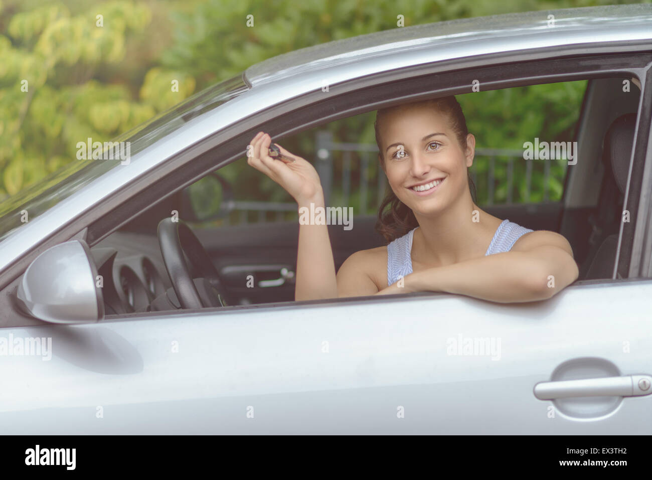 Junge hübsche Frau sitzt in ihrem Auto, lächelnd in die Kamera während zeigen, Schlüssel in die Hand. Stockfoto