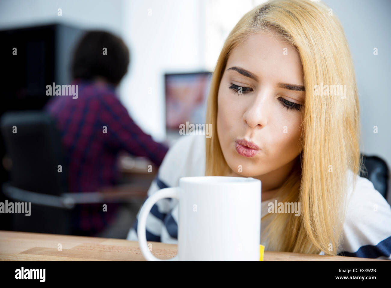 Junge Frau bläst auf einem Becher heißen Kaffee im Büro Stockfoto