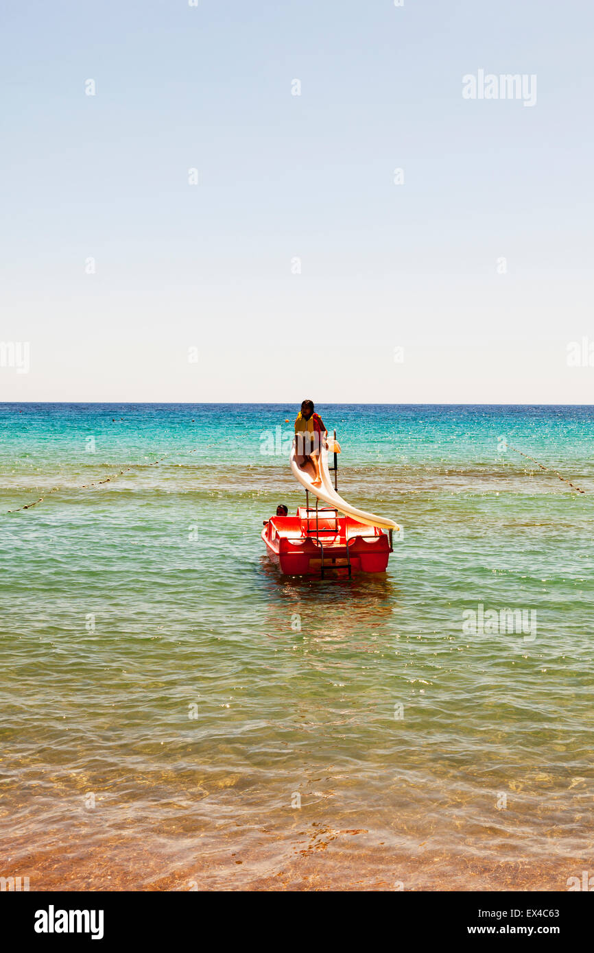 Junges Mädchen auf Wasserrutsche im Meer Schwimmweste Weste tragen, Wasserrutsche hinunter Stockfoto
