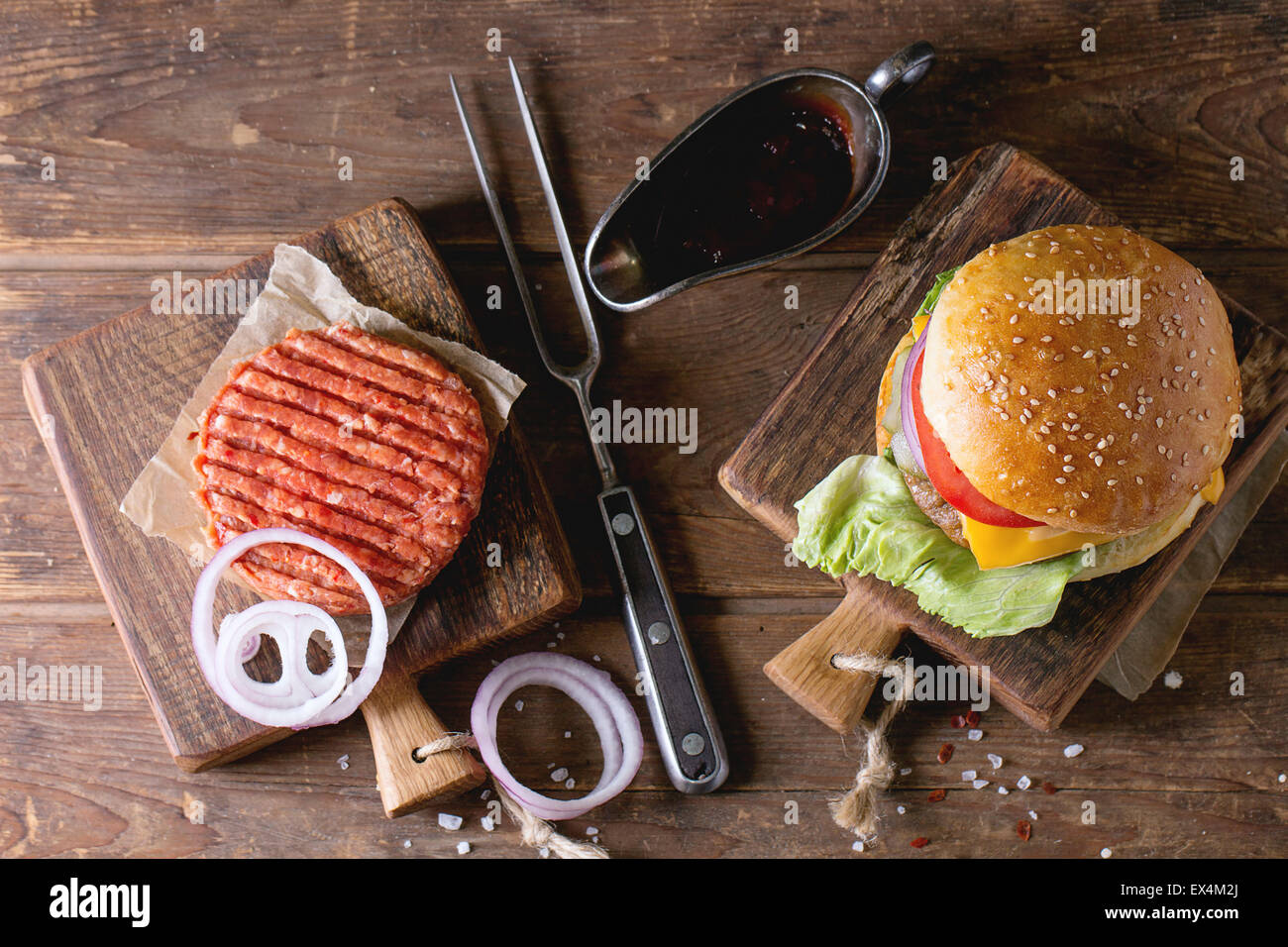 Frische hausgemachte Burger auf kleinen Schneidebrett und rohe Schnitzel und in Scheiben geschnittene Zwiebel, serviert mit Ketchup-Sauce und Fleisch Gabel über Holz Stockfoto