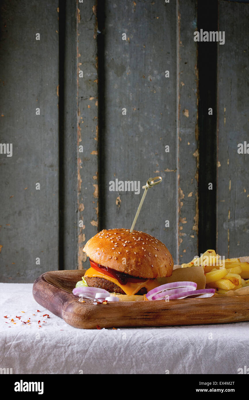 Holzplatte mit frischen hausgemachten Burger und gegrillte Kartoffeln über weiße Tischdecke mit grauem Hintergrund aus Holz. Dunkel rustikalen styl Stockfoto