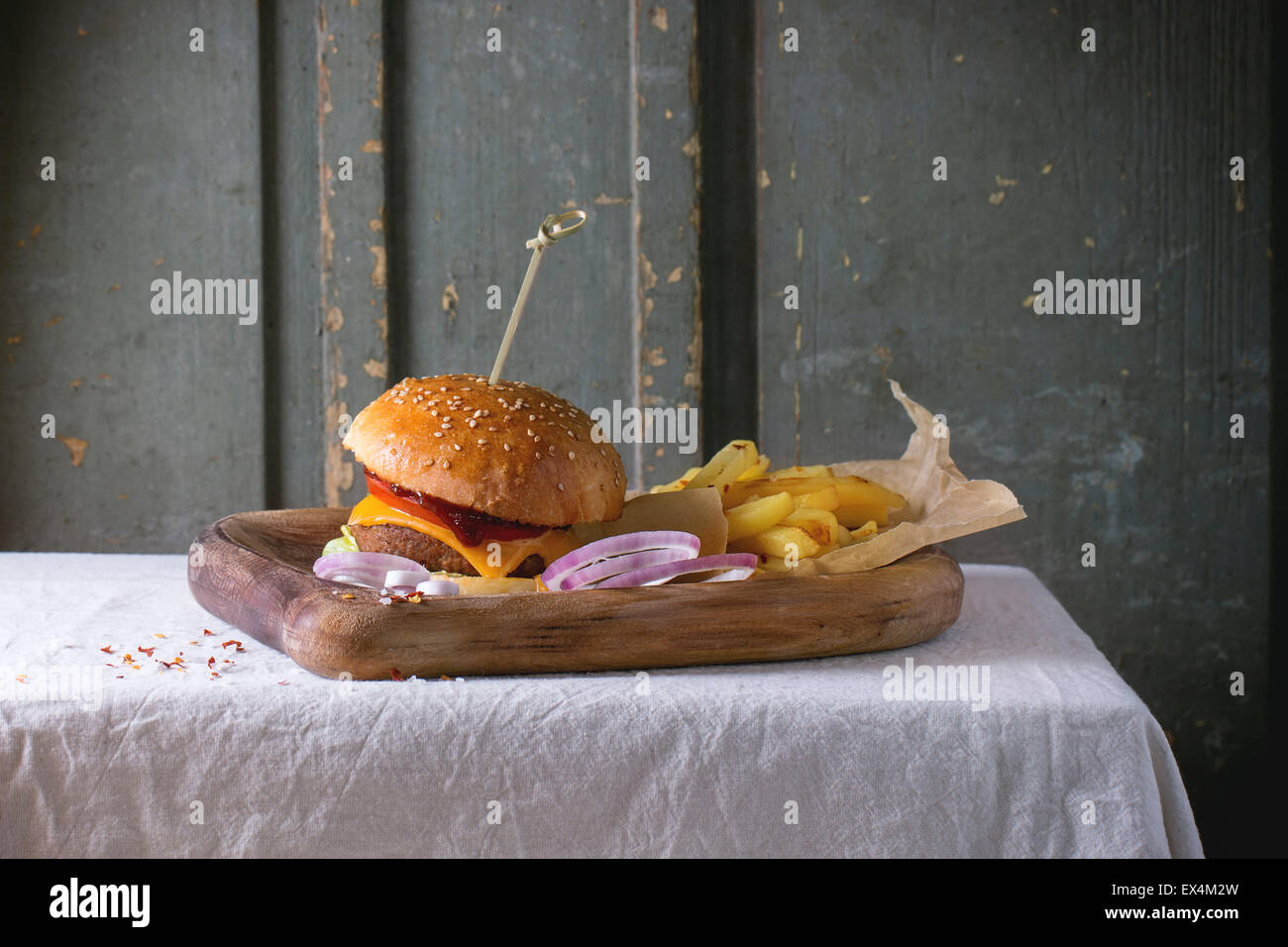 Holzplatte mit frischen hausgemachten Burger und gegrillte Kartoffeln über weiße Tischdecke mit grauem Hintergrund aus Holz. Dunkel rustikalen styl Stockfoto