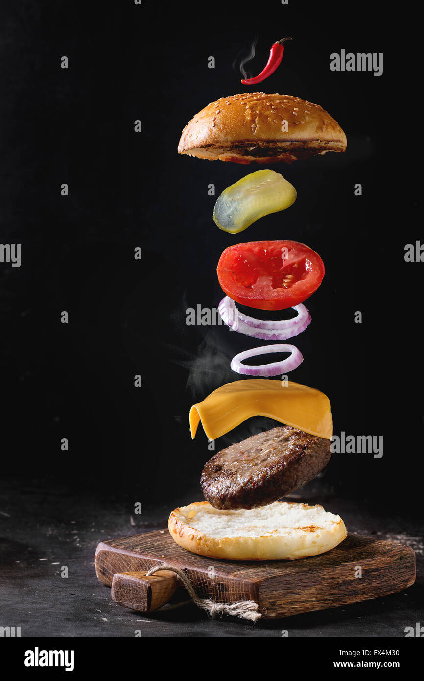 Zutaten für hausgemachte Burger auf kleinen Holzbrett über dunklen Hintergrund fliegen. Stockfoto