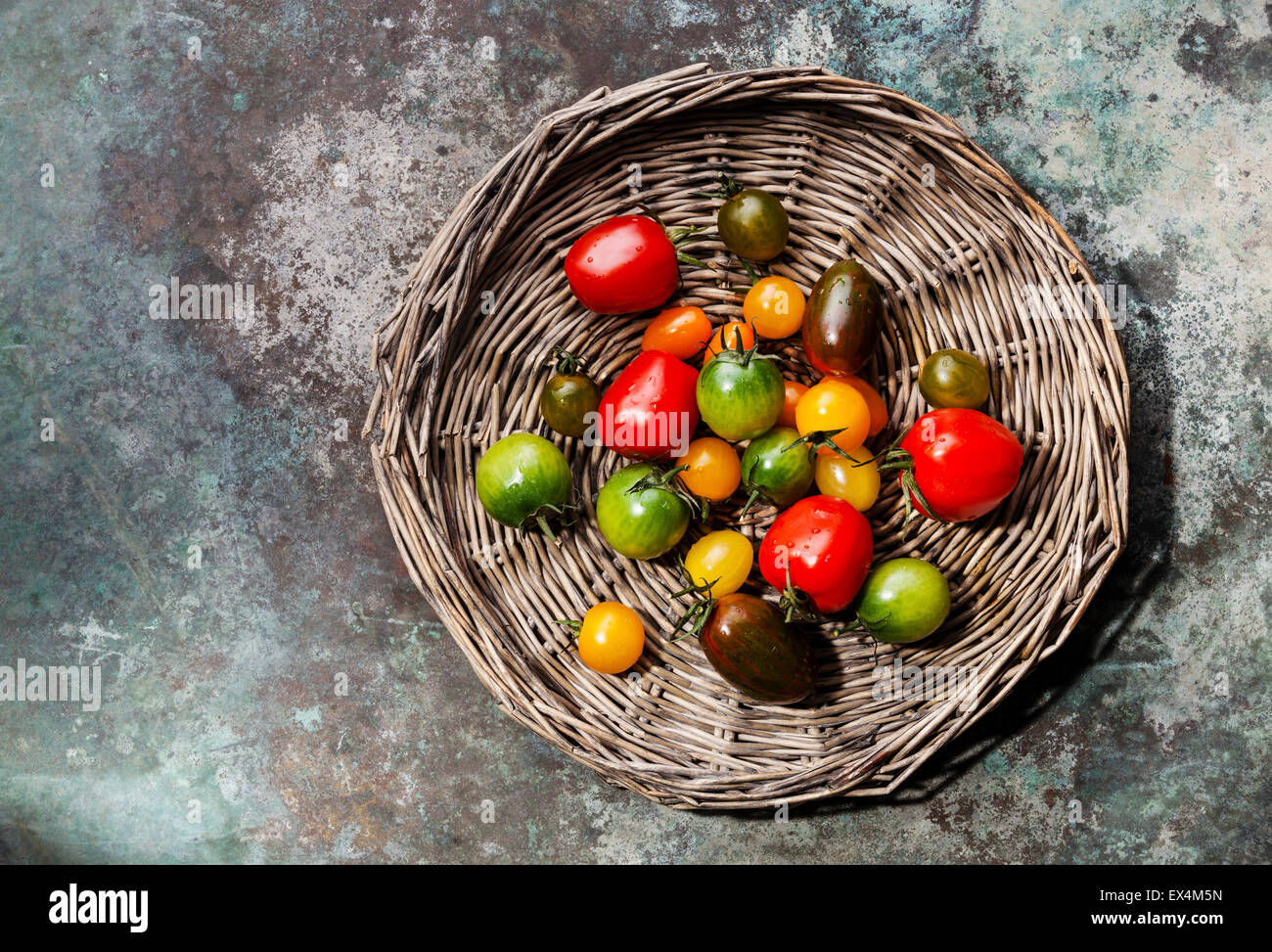 Reife frische bunte Tomaten auf Korbwaren Tablett auf Metall Hintergrund Stockfoto