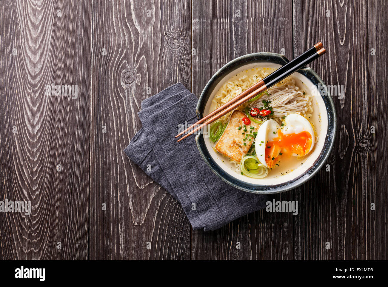 Asiatische Nudeln mit Ei, Tofu und Enoki in Schüssel auf grauem Hintergrund aus Holz Stockfoto