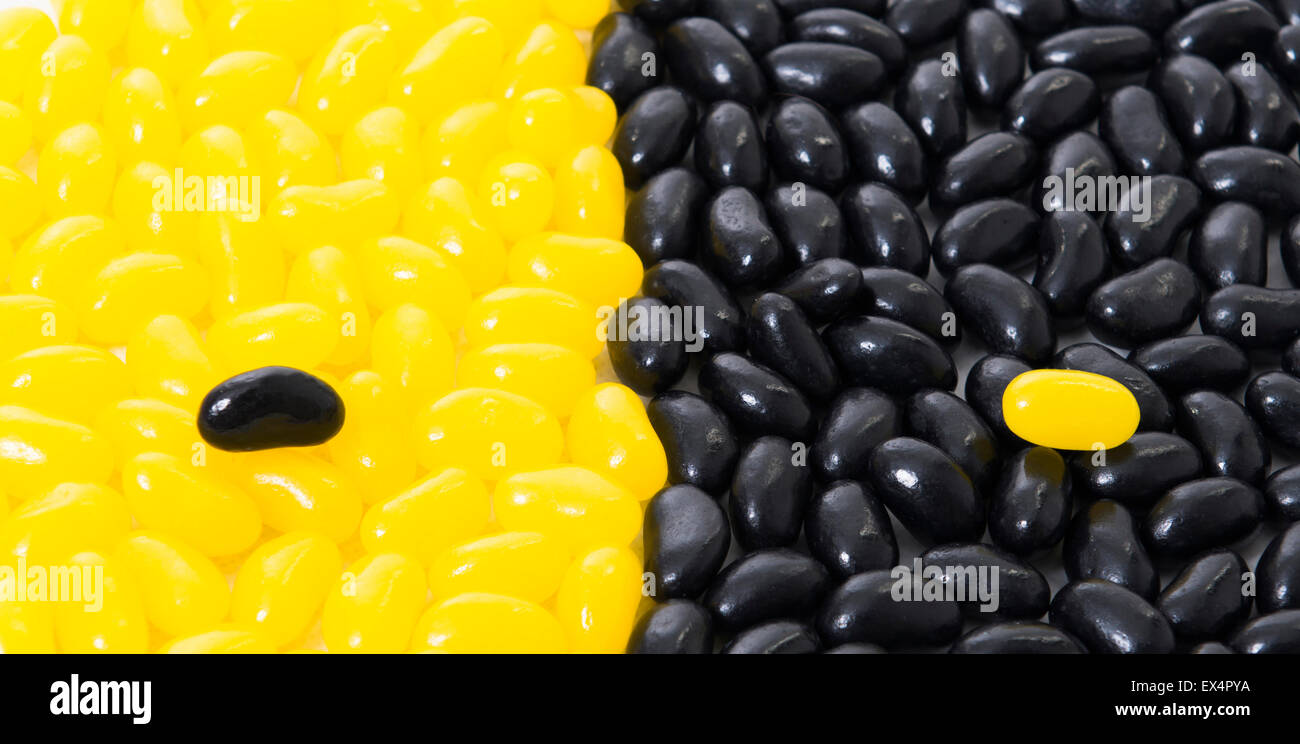Viele der schwarz-gelben Geleebohnen nebeneinander mit einem Jellybean jeder Farbe auf die andere Farbe. Stockfoto