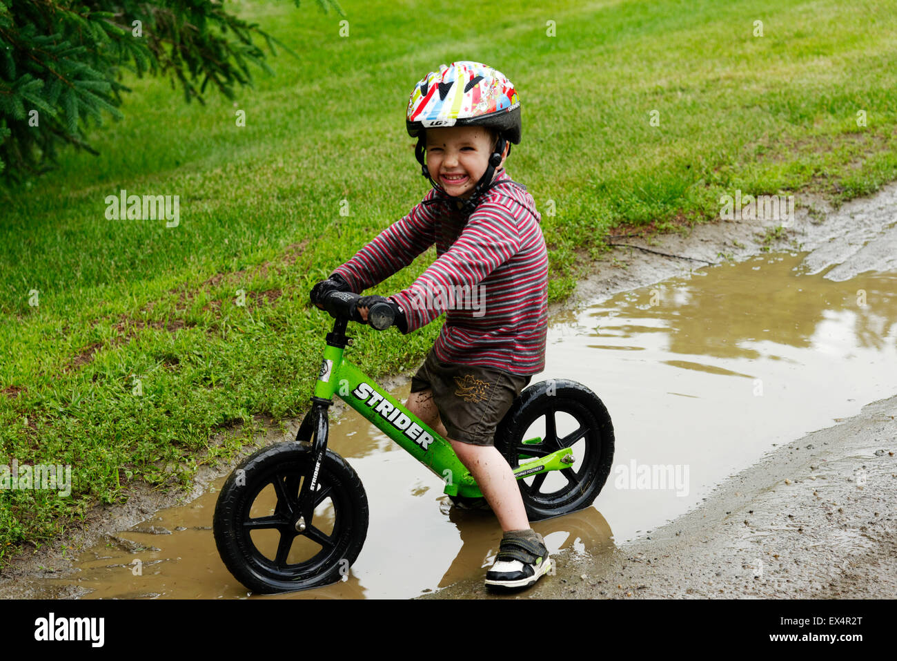 Ein kleiner Junge (3 Jahre) mit dem Balance-Fahrrad durch eine schlammige Pfütze Stockfoto