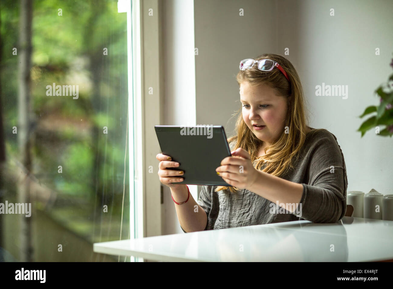 Teenager-Mädchen mit einem Tablet in der Nähe der Fenster im Haus sitzen. Stockfoto