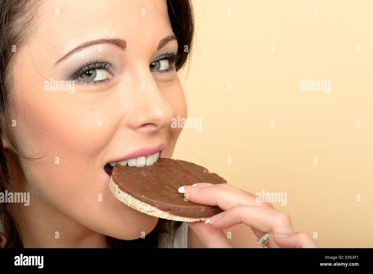 Attraktive schöne junge Frau, die einen einzigen Milch Schokolade überdachten Reis Kuchen Keks essen Stockfoto