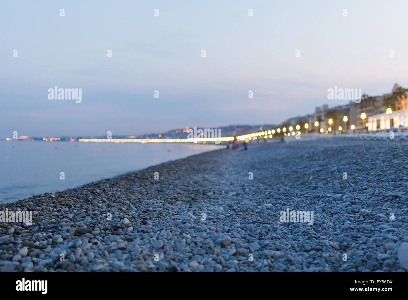 Beleuchtete Strandpromenade in der Nacht in Nizza mit unscharfen Menschen spielen im Hintergrund mit Fokus auf dem Kies Stockfoto