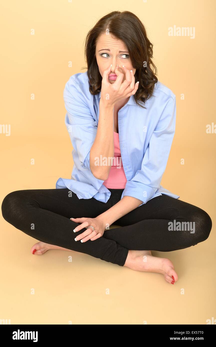 Attraktive junge Frau sitzt auf dem Boden trug ein blaues Hemd und schwarze Leggings ziehen dumme Mimik und handeln Stockfoto