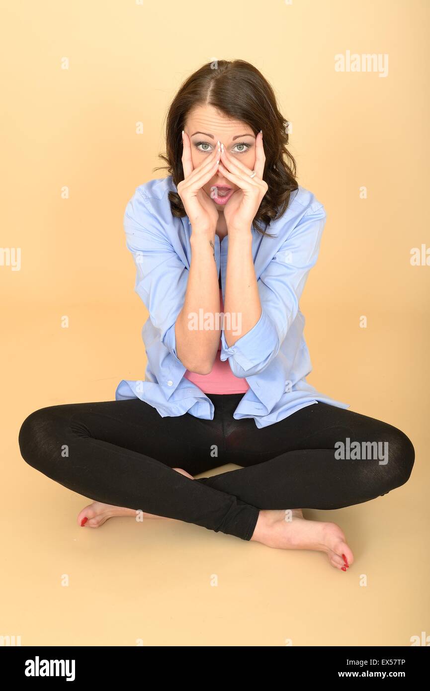 Attraktive junge Frau sitzt auf dem Boden trug ein blaues Hemd und schwarze Leggings ziehen dumme Mimik und handeln Stockfoto