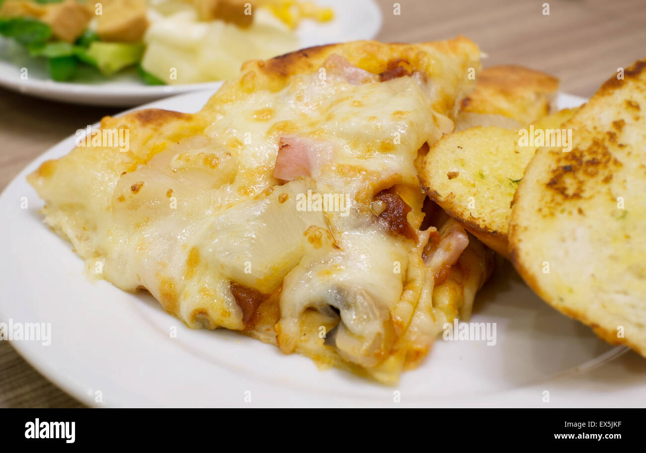 Detailansicht der eine appetitliche Schinken und Ananas italienische Pizza mit Knoblauchbrot und Salat Stockfoto