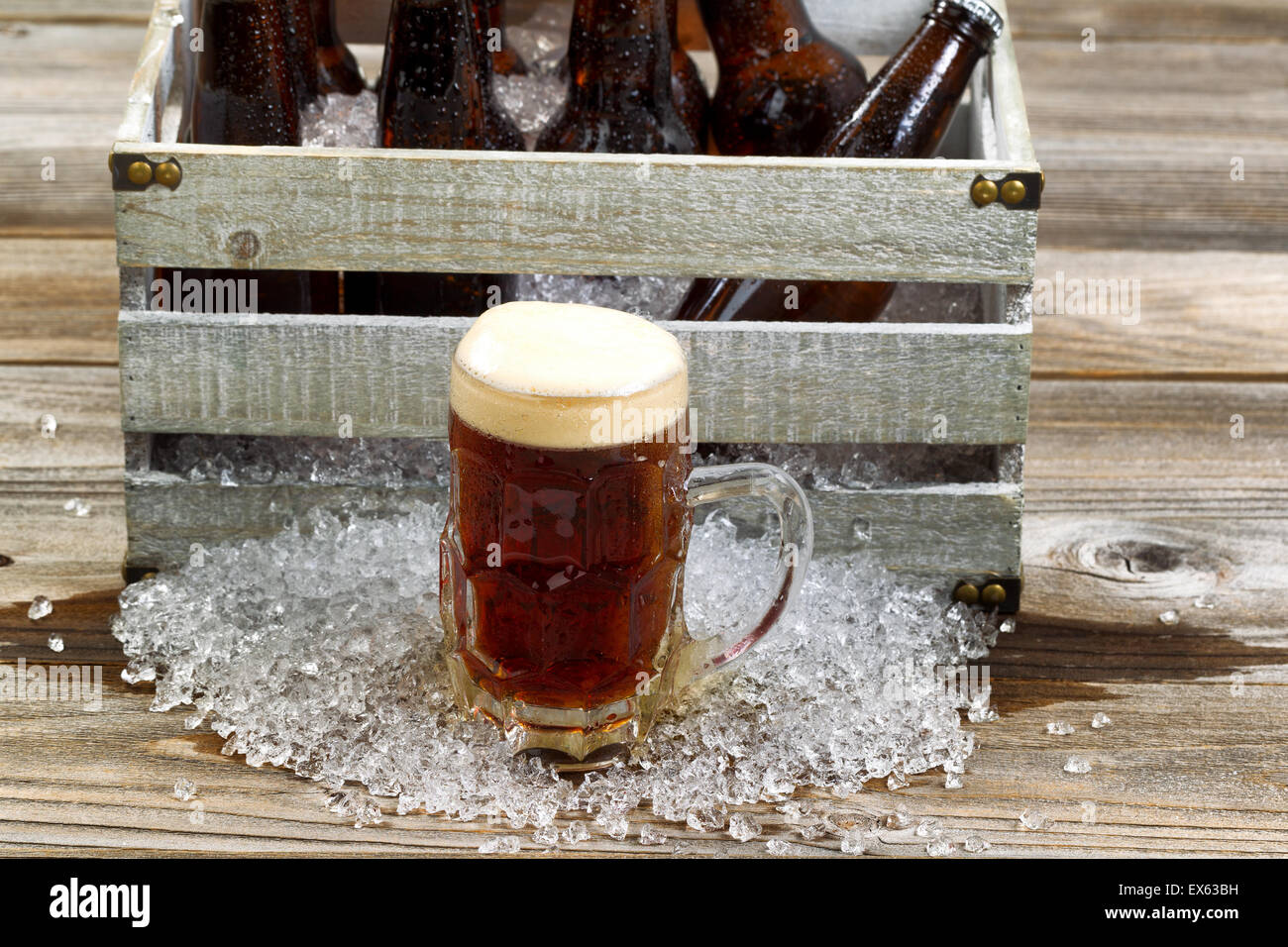 Frostigen Glas Tasse dunkles Bier, Fokus auf Vorderseite mit Vintage Kiste gefüllt mit Flaschenbier und Eis auf rustikalen hölzernen Wildschwein Stockfoto