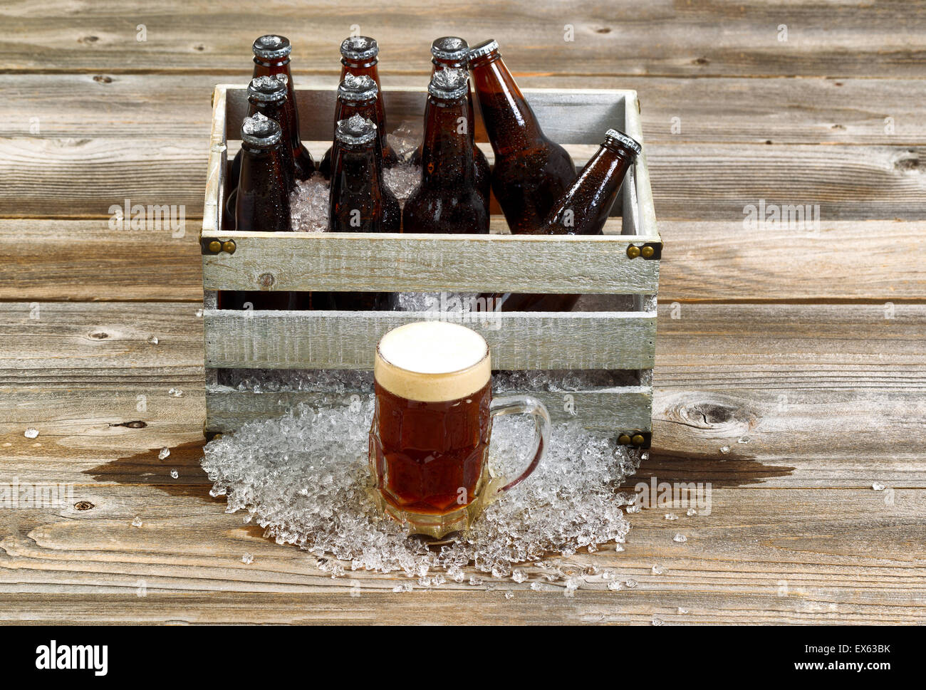 Blick nach vorne auf eine frostige großes Glas Tasse dunkles Bier mit Vintage Kiste gefüllt mit Flaschenbier und Eis auf rustikal aus Holz Stockfoto