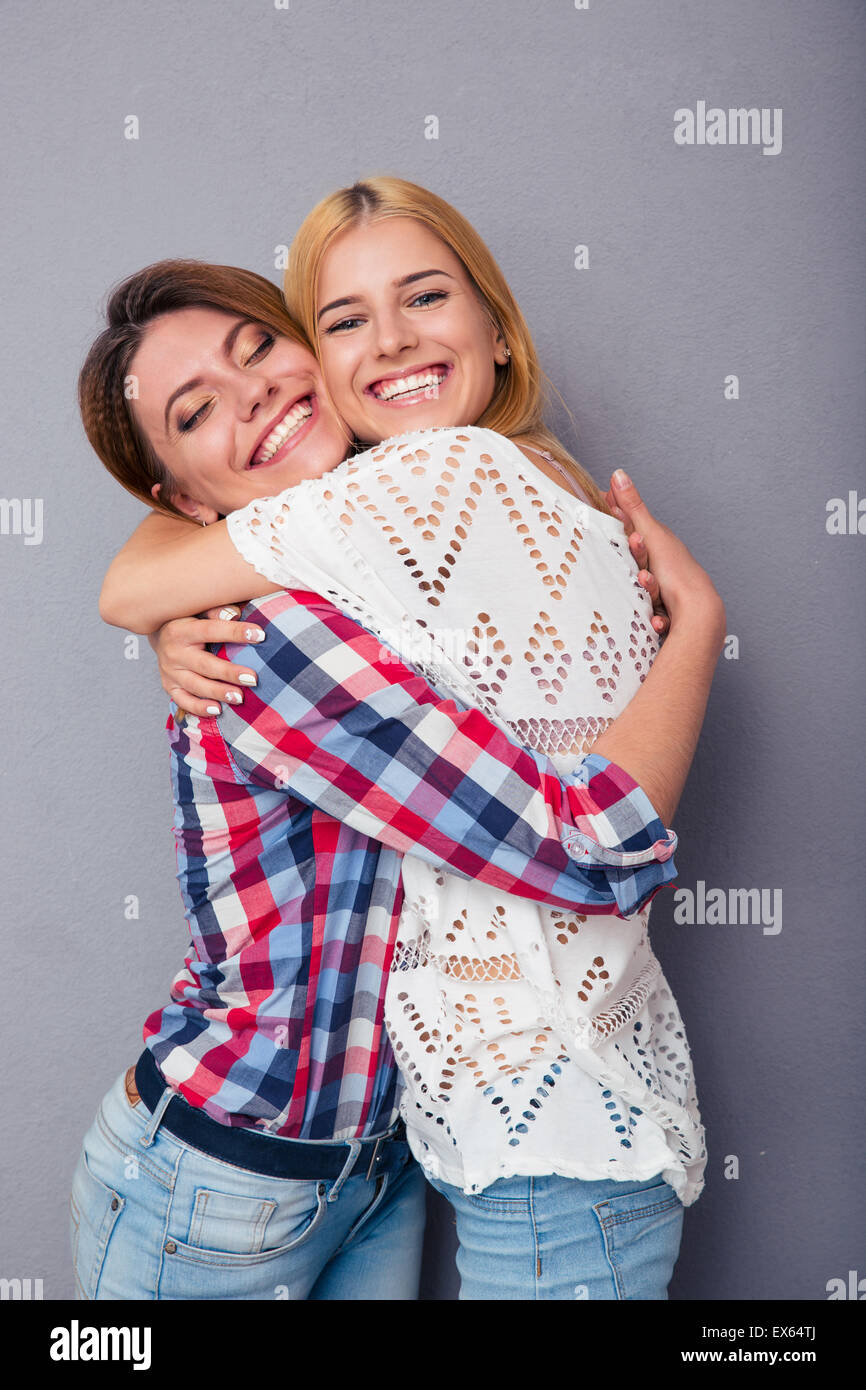 Glücklich zwei Mädchen umarmt auf grauem Hintergrund Stockfoto