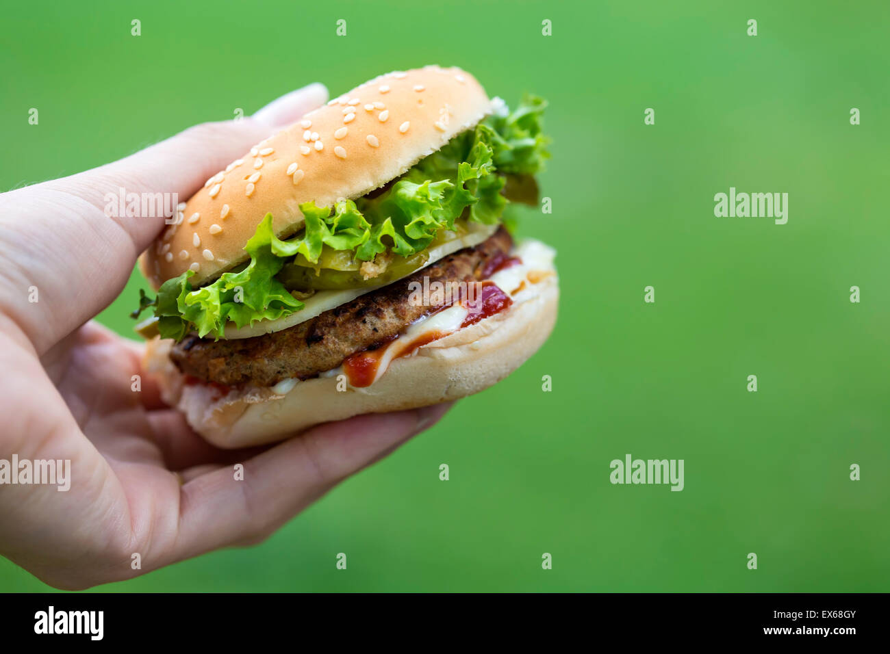 Cheeseburger in der Hand auf grünem Hintergrund mit Textfreiraum Stockfoto