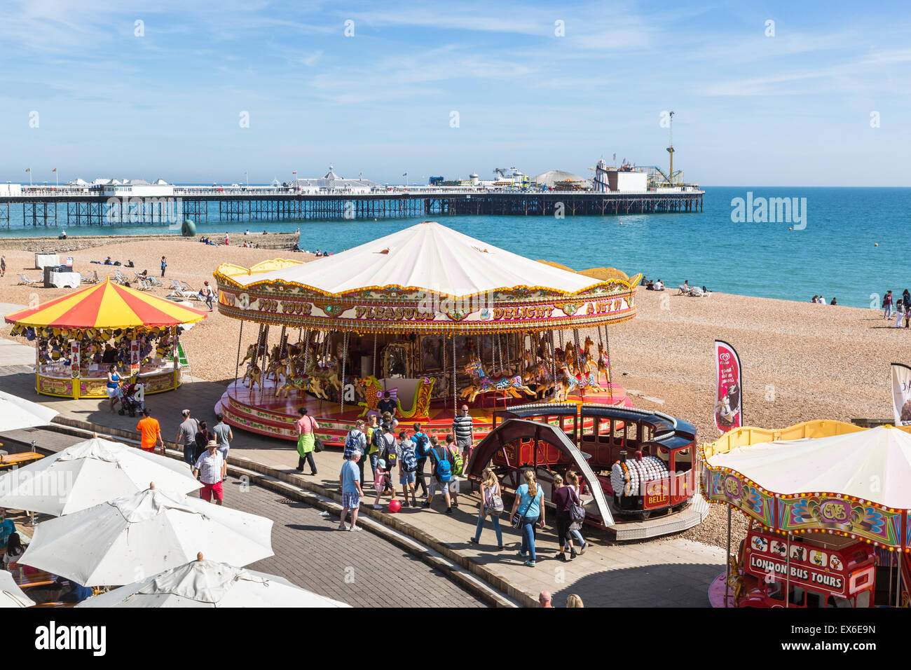 Direkt am Meer-Karussell und Kirmes Stände am Strand an einem sonnigen Sommertag in Brighton, East Sussex, Großbritannien und Palace Pier Stockfoto